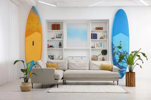 SUP boards, shelving unit with different decor elements and stylish sofa in.. Stock Photos