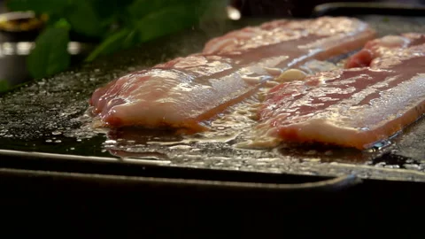 Super close-up of bacon strips roasting and sizzling on the flat grill Stock Footage 129388945