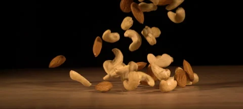 Super slow-motion of almonds and cashews fall on wooden table Stock Footage 323440044