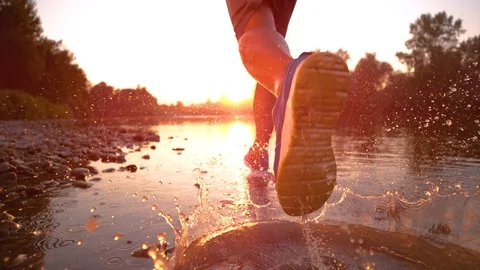 SUPER SLOW MOTION: Athletic man runs in the shallow stream towards the sunset. Stock Footage 101700025