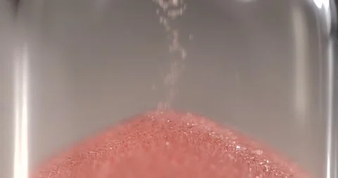 Super slow motion, Closeup Of Soft Pink Grains Flowing In Hourglass Under Warm Stock Footage 330110678
