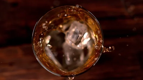 Super slow motion of falling ice cube into whiskey glass, top view. Stock Footage 90900631