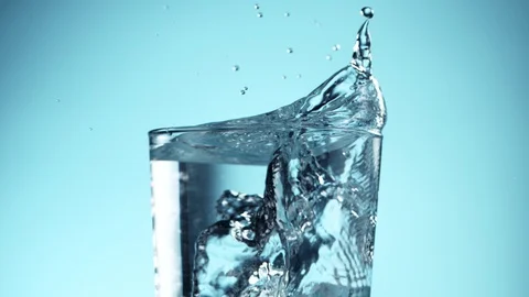 Super slow motion of falling ice cubes into glass of water on blue background. Stock Footage 128227843