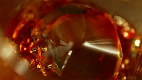 Super slow motion of falling ice cube into whiskey in super macro shot. Video stock 157674875