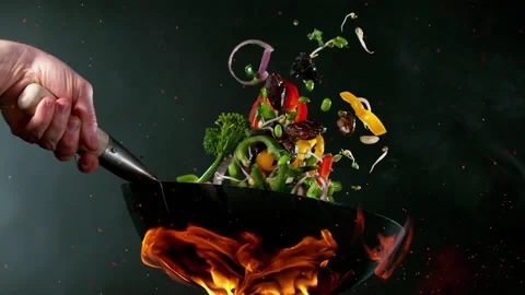 Super slow motion of flying sliced vegetable pieces from wok pan.