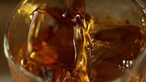 Super Slow Motion Macro Shot of Pouring Whiskey into Glass with Ice Cubes at Video stock 118749600