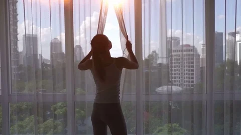 Super slow motion. Young woman uncover the big window and looking out her Stock Footage
