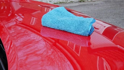 Super soft blue microfiber towel on a red car hood being pick up - medium shot Stock Footage 321063000