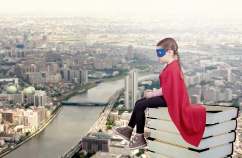 Superhero kid sitting on a stack of books against urban background Fotos de archivo