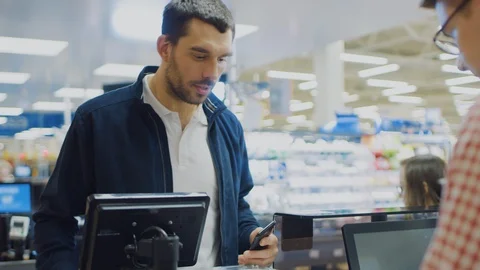 At the Supermarket: Checkout Counter Customer Pays with Smartphone for His Food Stock Footage