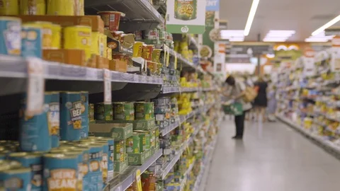 Supermarket shopping aisle woman shops in background with stacked food cans Stock Footage