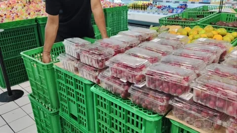 A supermarket worker arranging plastic containers of fresh red grapes Stock Footage 337781067