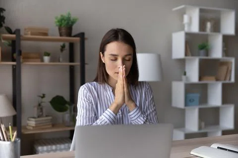 Superstitious young woman worker pray at workplace Stock Photos