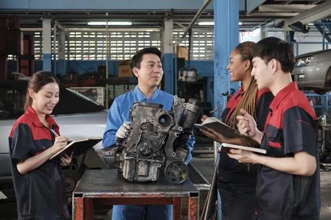 Supervisor engineer is teaching mechanic workers about car engines at a garage. Stock Photos