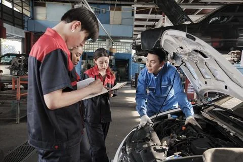 Supervisor engineer is teaching mechanic workers about car repair at a garage. Stock Photos