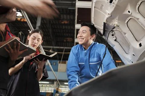 Supervisor engineer is teaching mechanic workers about car repair at a garage. Stock Photos