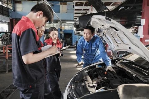 Supervisor engineer is teaching mechanic workers about car repair at a garage. Stock Photos