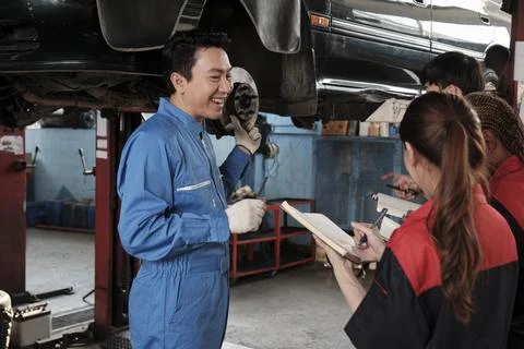 Supervisor engineer is teaching mechanic workers about car repair at a garage. Stock Photos