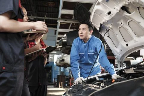 Supervisor engineer is teaching mechanic workers about car repair at a garage. Stock Photos