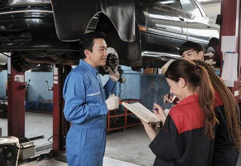 Supervisor engineer is teaching mechanic workers about car repair at a garage. Stock Photos