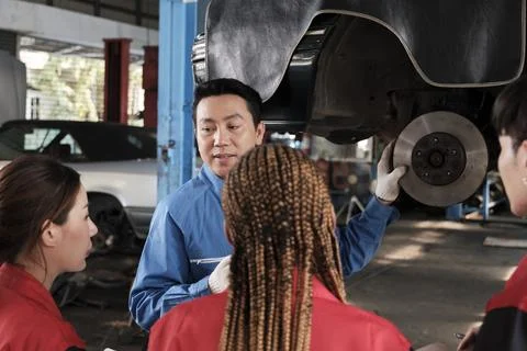Supervisor engineer is teaching mechanic workers about car repair at a garage. Stock Photos