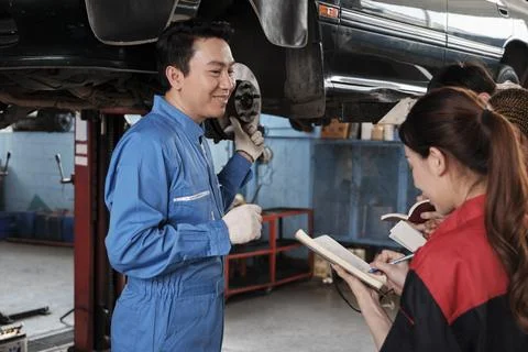 Supervisor engineer is teaching mechanic workers about car repair at a garage. Stock Photos
