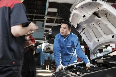 Supervisor engineer is teaching mechanic workers about car repair at a garage. Stock Photos