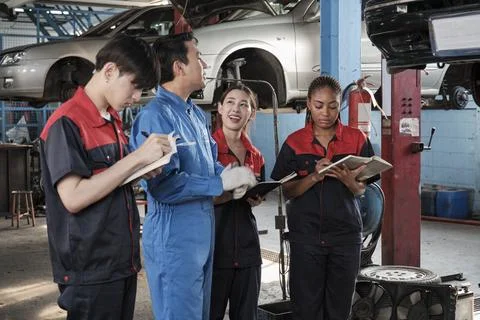 A supervisor engineer is training mechanic workers about car repair at a garage. Stock Photos