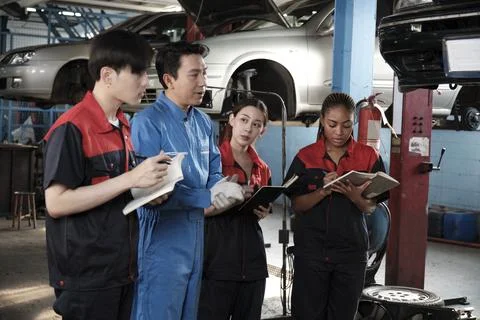 A supervisor engineer is training mechanic workers about car repair at a garage. Stock Photos