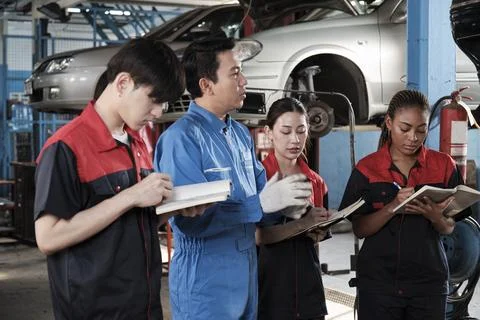 A supervisor engineer is training mechanic workers about car repair at a garage. Stock Photos