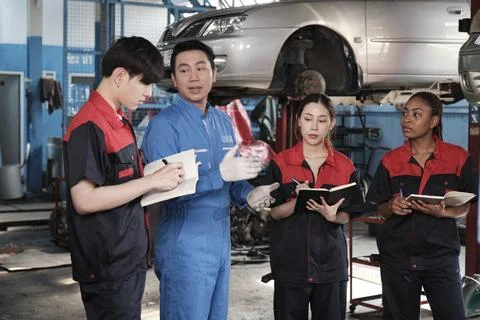 A supervisor engineer is training mechanic workers about car repair at a garage. Foto stock