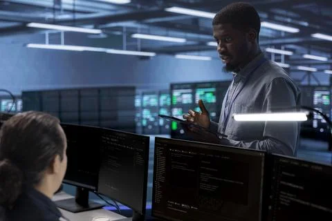 Supervisor in server room overseeing employee repairing equipment Foto stock