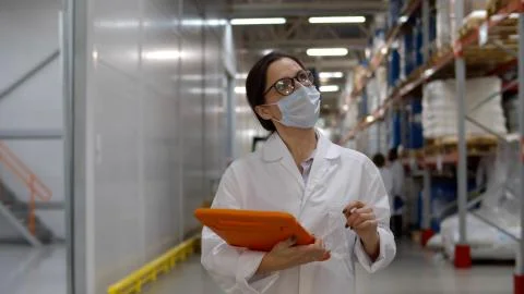 Supervisor in uniform and mask using tablet for checking data while standing in Foto stock