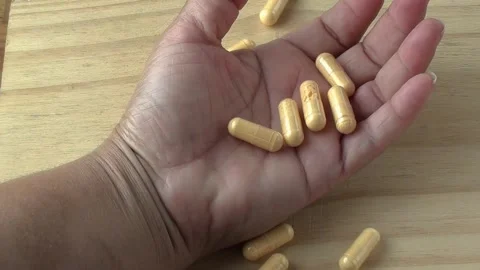Supplement yellow capsules falling into a woman's palm hand Stock Footage 251388233