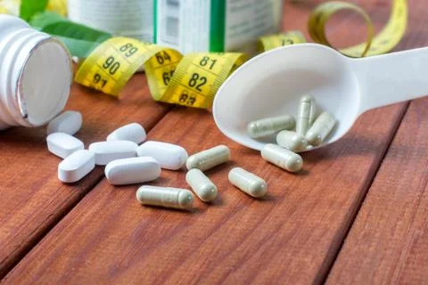 Supplements capsules spill out of a plastic spoon on a wooden table Stock Photos
