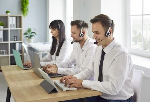 Support agents with headsets working on laptops in a bright modern office Stock Photos