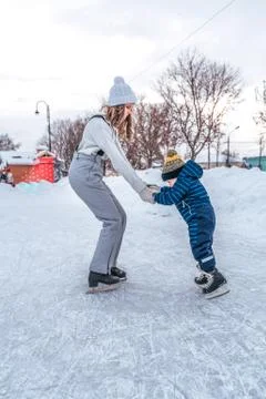 Support and first steps on skates. A young mother skates in the park in winter Stock Photos