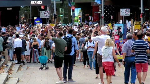 Supporters watch as thousands of demonstrators walk along a city street. Video stock 129479324