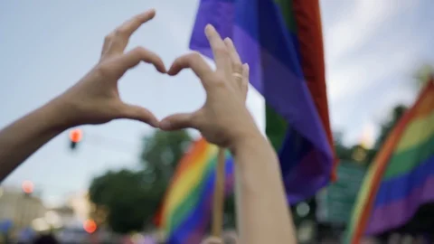 Supporting hands make heart sign and wave in front of a rainbow flag flying on t Stock Footage 111904176