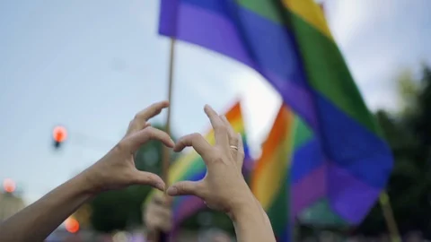 Supporting hands make heart sign and wave in front of a rainbow flag flying  Stock Footage 111904178