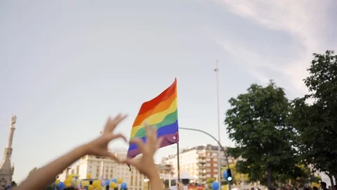 Supporting hands make heart sign and wave in front of a rainbow flag flying  Stock Footage 111904182