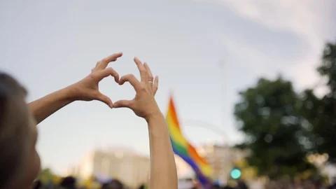 Supporting hands make heart sign and wave in front of a rainbow flag flying Stock Footage 111904183