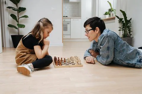 Supportive dad teaching chess to his child daughter, they play on the floor Stock Photos