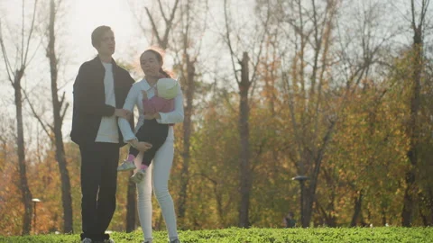 Supportive parents assist toddler with first steps outdoors. Family celebrates Stock Footage 334629573
