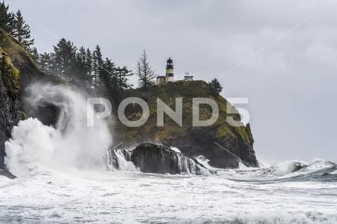 Surf fills the air with salt spray at Cape Disappointment with a lighthouse up o Stock Photos