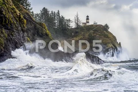 Surf fills the air with salt spray at Cape Disappointment with a lighthouse up o Stock Photos