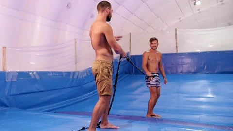 Surf instructor gives lesson to young guy on wave simulator indoors. Young Stock Footage 212362460
