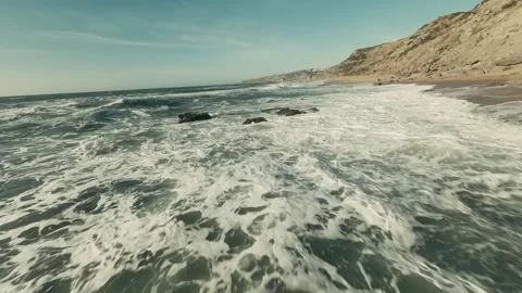 Surf rolls into sandy beach with rugged cliffs Video stock 341826036