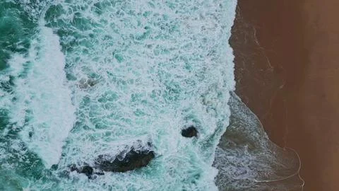Surf waves create foam patterns at sandy beach top view. Texture of seafoam Stock Photos
