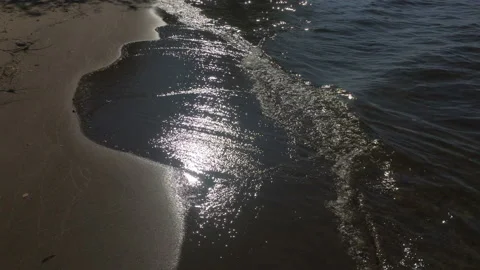 Surf waves in the sand. Walk along the beach. Sun rays reflected in the waves. Stock Footage 115796202